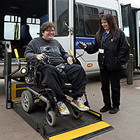Person in a wheelchair leaving a Metro Mobility van with help from driver.